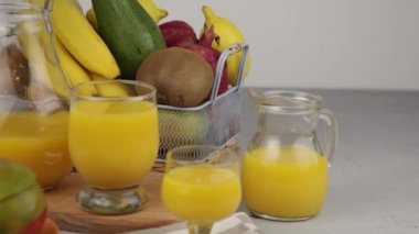 Bir bardak meyve suyu. Sarı ferahlatıcı yaz içkileri. Taze mango suyu, portakal suyu. Meyve sepeti masanın üstünde. Mutfakta taze meyve ve meyve suyu var. Vejetaryen yemeği. Vitamin içeceği. Muz, kivi, limon.