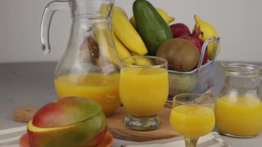 Bir bardak meyve suyu. Sarı ferahlatıcı yaz içkileri. Taze mango suyu, portakal suyu. Meyve sepeti masanın üstünde. Mutfakta taze meyve ve meyve suyu var. Vejetaryen yemeği. Vitamin içeceği. Muz, kivi, limon.