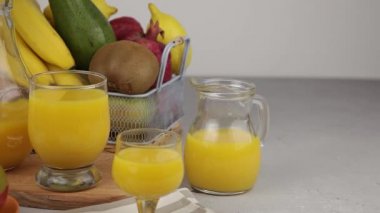Bir bardak meyve suyu. Sarı ferahlatıcı yaz içkileri. Taze mango suyu, portakal suyu. Meyve sepeti masanın üstünde. Mutfakta taze meyve ve meyve suyu var. Vejetaryen yemeği. Vitamin içeceği. Muz, kivi, limon.
