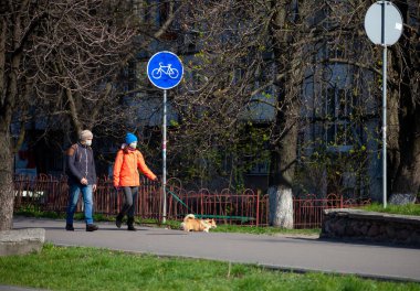 Kyiv, Ukrayna - 11 Nisan 2020: Karantina sırasında sokakta köpek gezdiren maskeli adam ve kadın. Koruyucu maskeli insanlar. Coronavirus salgını sırasında şehrin sokakları.
