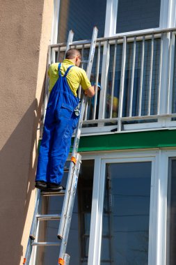 Merdivenlerde duran bir adam caddenin camlarını siler. Temizlik şirketi. Mavi tulumlu işçi, çok katlı bir apartmanın camını yıkıyor..