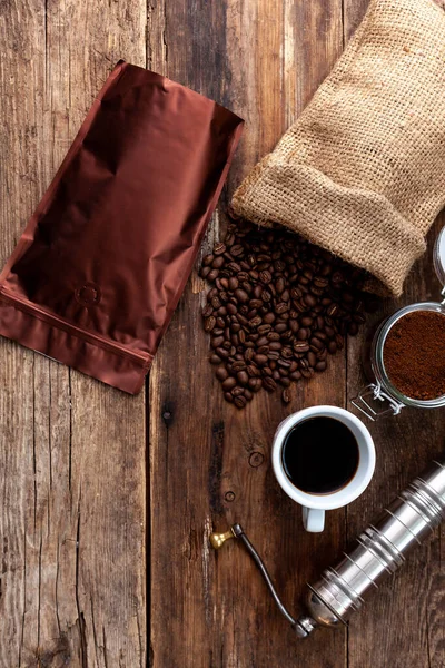 Bag of coffee on a wooden table. Coffee beans and ground in a jar. Manual coffee grinder. Top view, place for text. Brown background. Packing coffee in a pack. Cup with a drink.