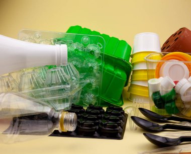 Çöpleri ayıklıyorum. Geri dönüşüm için plastik atık. Plastik şişeler, kaplar, kabartma tozu, çatallar, kaşıklar, yumurta ambalajları, kapaklar. Metin için karşılanan sarı arkaplan. Çevre dostu - sıfır atık.