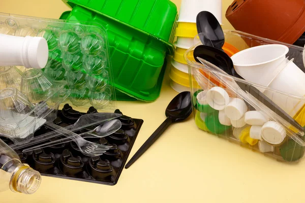 Sorting garbage. Plastic waste for recycling. Plastic bottles, containers, baking soda, forks, spoons, egg packaging, caps. Yellow background with met for text. Eco friendly - zero waste.