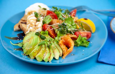 Kahvaltınız mavi tabakta. Avokado, kırmızı balık somonu, yumurta, susam, keten, domates, mikroyeşil salat. Mesaj için yeri olan mavi arkaplan. Sağlıklı yemek, sağlıklı yemek..