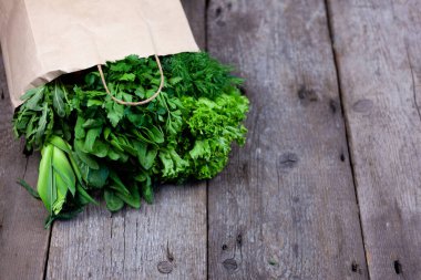 Kese kağıdında taze yeşiller. Yeşil soğan, dereotu, maydanoz, ıspanak, roka, doru. Eve yiyecek ve taze sebze teslimatı. Metin için yeri olan tahta arkaplan.