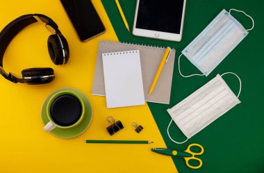 Evde çalışıyorum. Masaüstünde tıbbi maske var. Uzaktan çalışma ve çalışma. Telsiz işi, serbest çalışma. Mesajlar için yer ve notlar için kalem olan not defteri. Yerleşim planı. Masaüstü, çalışma alanı düzlüğü. Ofis geçmişi