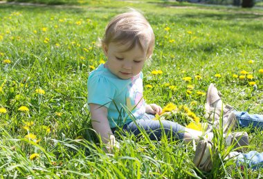Küçük kız çim üzerinde oturan ve havada oynuyor
