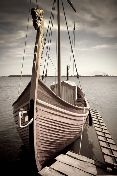A moored Viking boat with a dragonhead on a bow and an accommodation ladder. Low color saturation for a faded retro or vintage effect — Stock Photo, Image