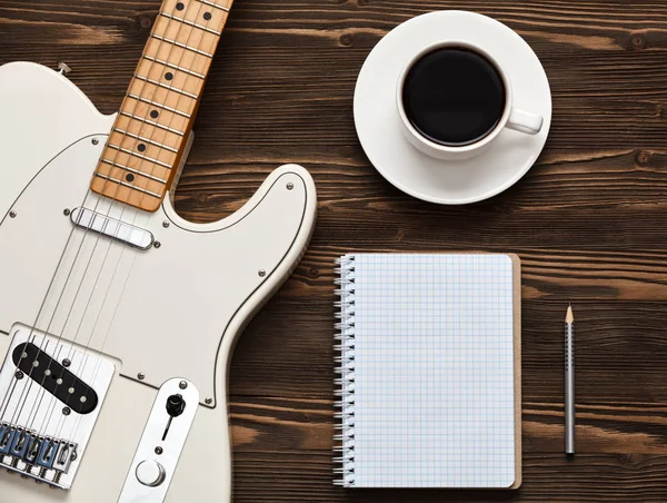 Coffee cup and guitar on wooden table.