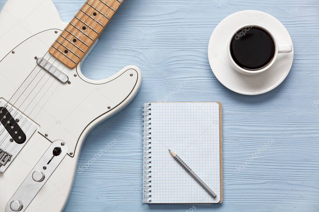 Coffee cup and guitar on wooden table.