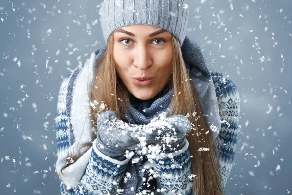 Navidad. Una chica con ropa de invierno soplando en la nieve . — Foto de Stock