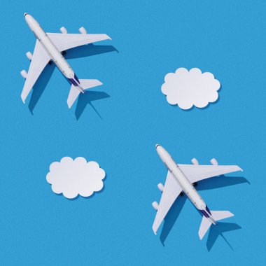 Miniature toy airplane on colorful paper background. Flat lay design of travel concept with plane and clouds on blue sky.
