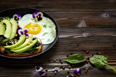 Avokadolu sandviç, ıspanak ve tavada kızarmış yumurta. Koyu kırsal ahşap arkaplan ve bir yazı için yer.