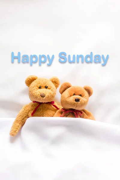 Teddybär liegt im weißen Bett mit der Botschaft "Happy Sunday"" — Stockfoto