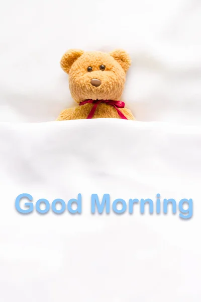 Teddybär liegt im weißen Bett mit der Botschaft "Guten Morgen " — Stockfoto