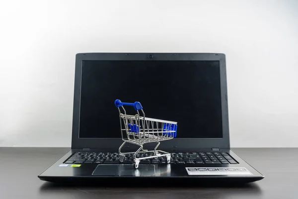 Computador notebook tela em branco com carrinho de compras na mesa de madeira — Fotografia de Stock