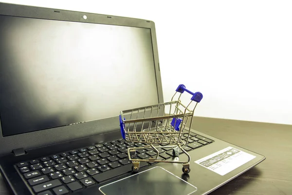 Computadora portátil pantalla en blanco con carrito de compras en mesa de madera — Foto de Stock