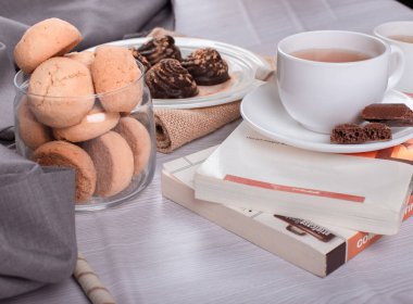 Kitap, tatlı atıştırmalıklar ve masada bir fincan çay.
