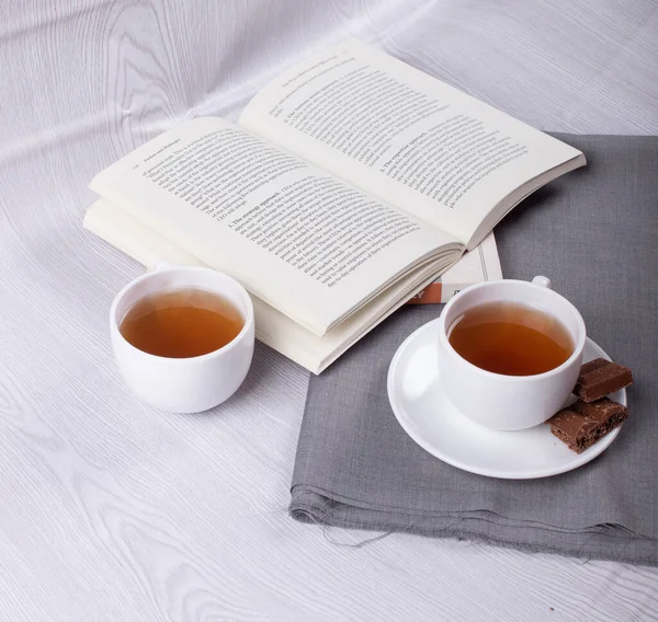 Boek, kopje thee en chocolade op tafel — Stockfoto