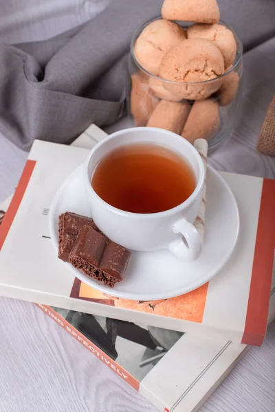 甘いお菓子、お茶とチョコレートのカップ、ライトバックの本 — ストック写真