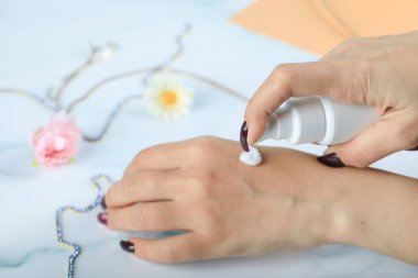 Mavi arka planda cilalı parmaklarıyla ellerine el kremi süren bir kadın.