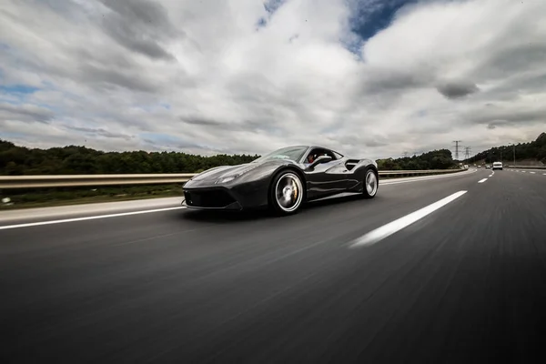 Siyah spor model araba bulutların altında gidiyor.