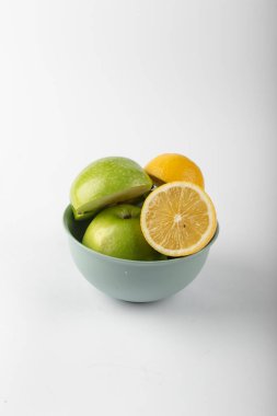Beyaz arka planda izole edilmiş gümüş bir kasede yeşil elma ve limon.