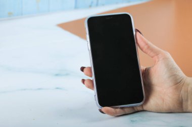 Elinde siyah bir cep telefonu tutuyor.