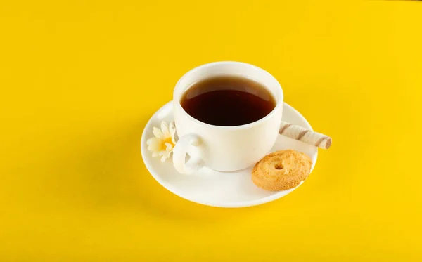 Чашка чая с печеньем на желтом фоне — стоковое фото