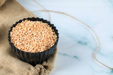 Çuval bezi üzerinde siyah plastik bir kasede sarı kuru fasulye.