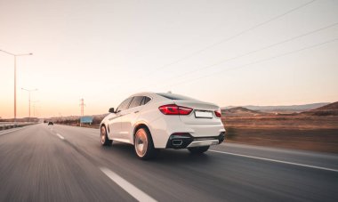 Kırmızı ksenon ışıklı beyaz sedan araba yolda gidiyor.