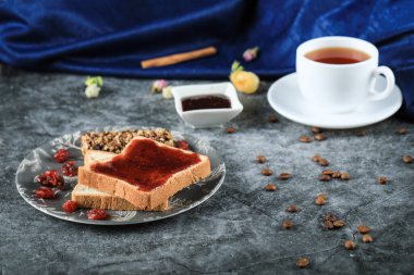 Bir fincan çay, çikolatalı tost ve mermer bir masada çilek reçeli.