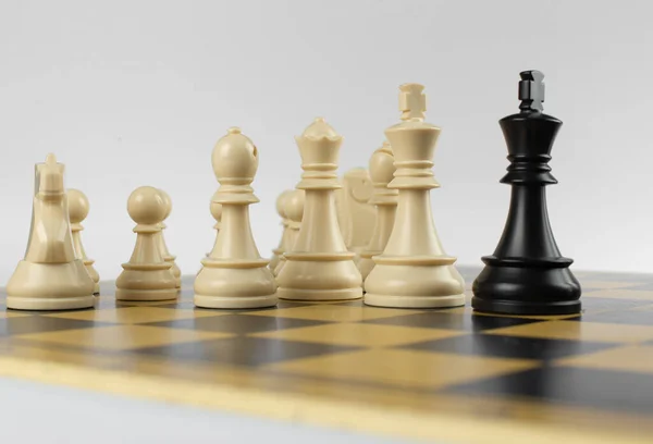 Białe postacie przeciwko czarnemu królowi na szachownicy na białym tle — Zdjęcie stockowe
