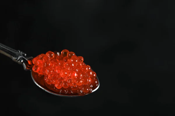 Roter Kaviar in einem metallischen Löffel isoliert auf schwarzem Hintergrund — Stockfoto