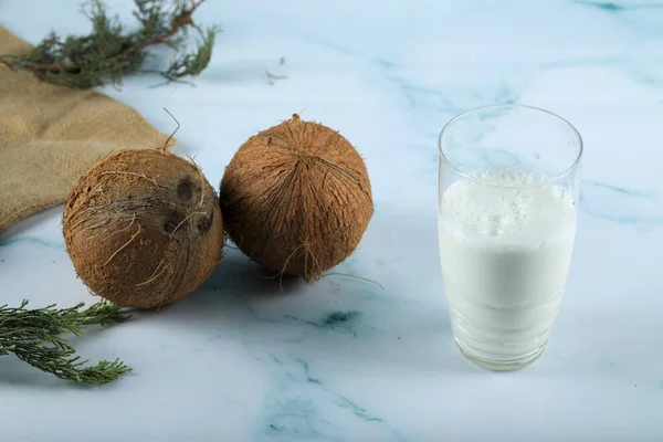 Braune Kokosnussfrüchte und ein Glas Milch isoliert auf blau — Stockfoto