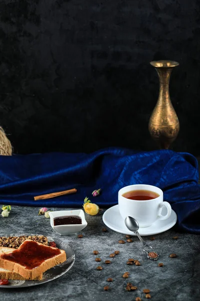 Хлебные тосты с ягодным джемом, коричные палочки и стакан чая на голубом столе — стоковое фото