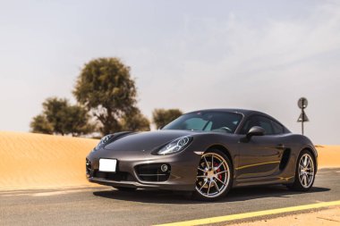 Çölde, güneşin altında gri renkli bir spor araba sürüyorum.