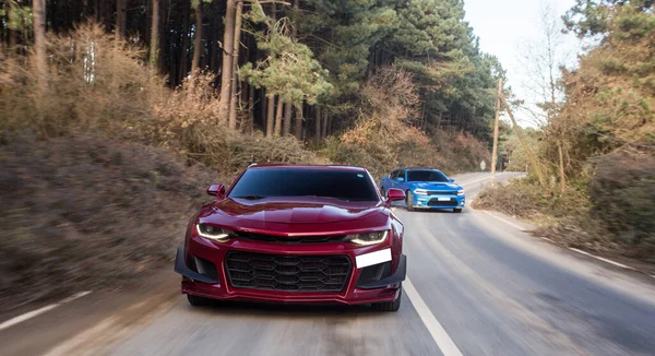 Rojo coche deportivo de lujo conduciendo a través del bosque con un coche azul justo detrás — Foto de Stock