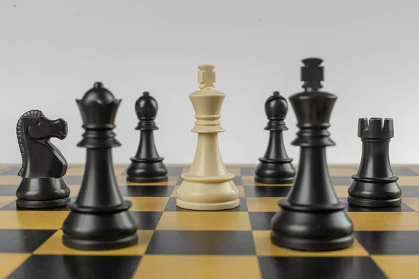 Figura blanca en el centro y negros alrededor en un tablero de ajedrez sobre fondo blanco aislado —  Fotos de Stock
