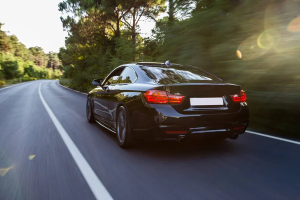 Black luxury sedan back view driving accross the forest