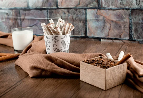 Coffee beans, waffle sticks and a glass of milk wrapped with a scarf on a wooden table — Stock Photo, Image