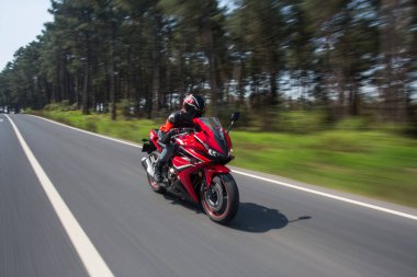 Orman yolunda kırmızı motosikletli bir motorcu.