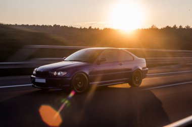 Siyah birinci sınıf araba güneş ışığının altında yolda.