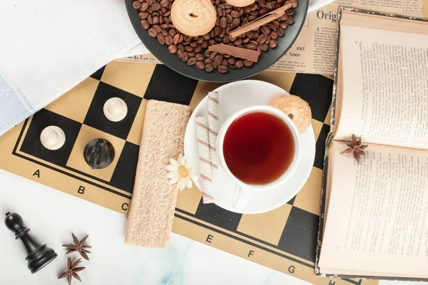 Eine Teetasse und ein Buch auf einem Schachbrett — Stockfoto