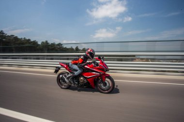 Kasklı motorcu mavi gökyüzünün altındaki köprüde motosiklet sürüyor.