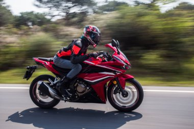 Orman yolunda kırmızı bir motosiklet sürmek, vites ve kaskla.