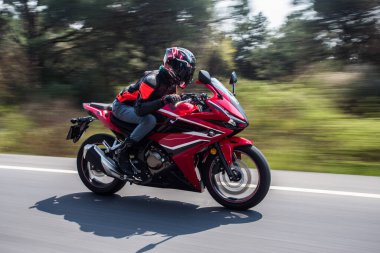 Orman yolunda yüksek hızda kırmızı bir motosiklet sürüyor. 