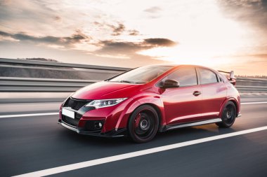 Güneşli bir havada kırmızı Coupe yolda gidiyor.