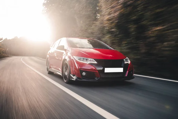 Kırmızı coupe güneş ışığının altında yolda gidiyor.